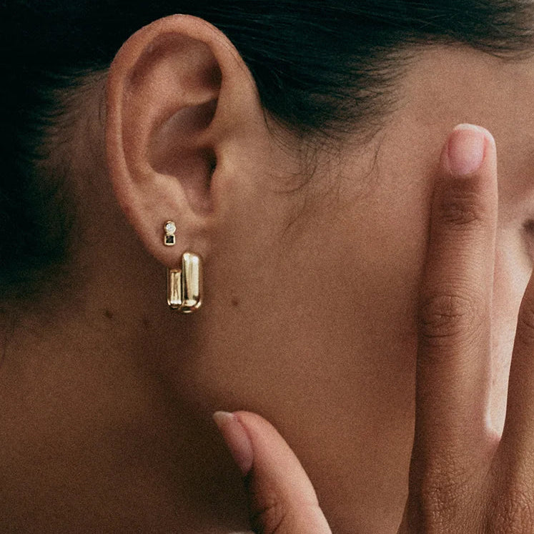 Close-up of a person wearing gold earrings and rings, with one hand covering their face.