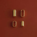 Four small gold-toned metal hardware pieces arranged in a 2x2 grid on a textured reddish-brown background.