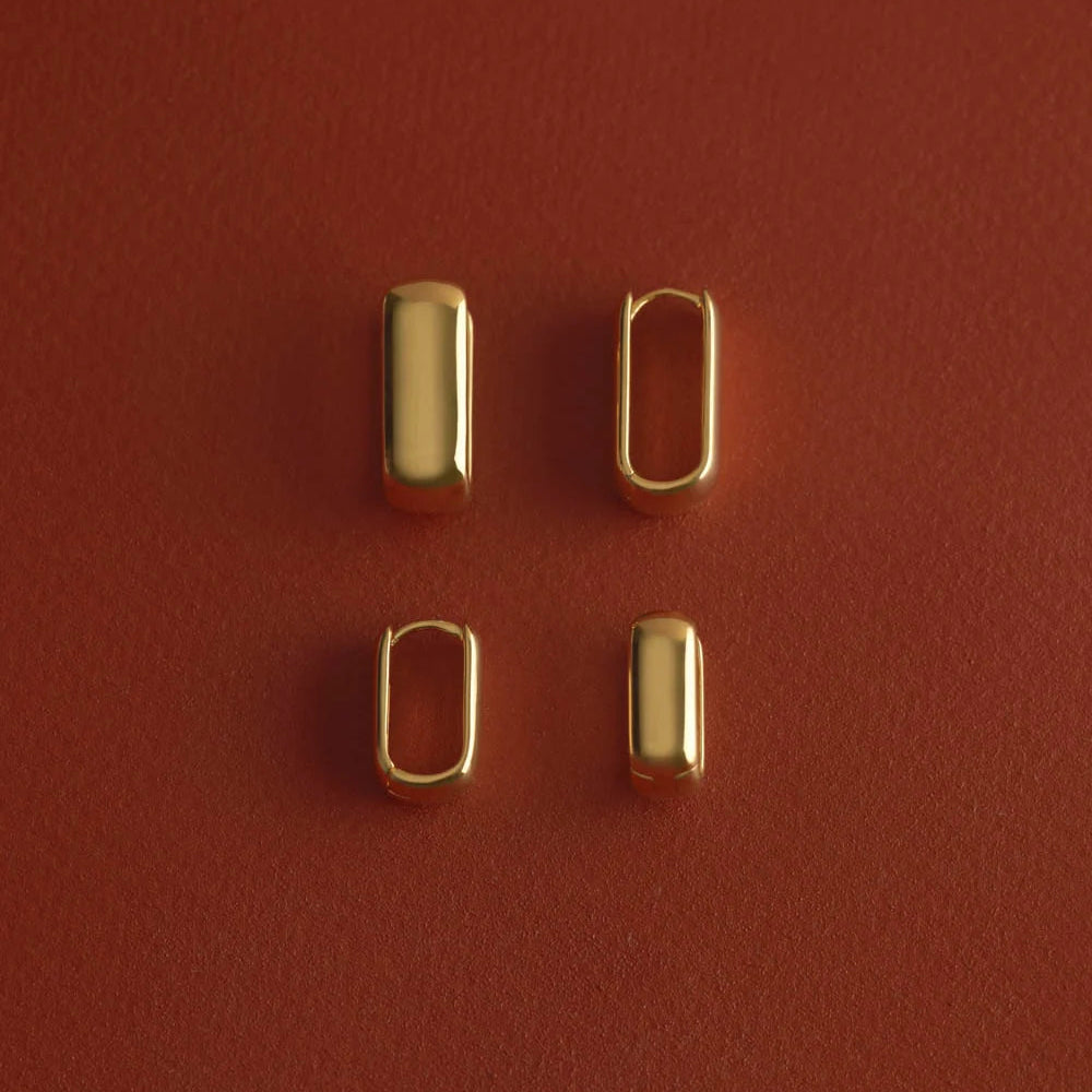 Four small gold-toned metal hardware pieces arranged in a 2x2 grid on a textured reddish-brown background.