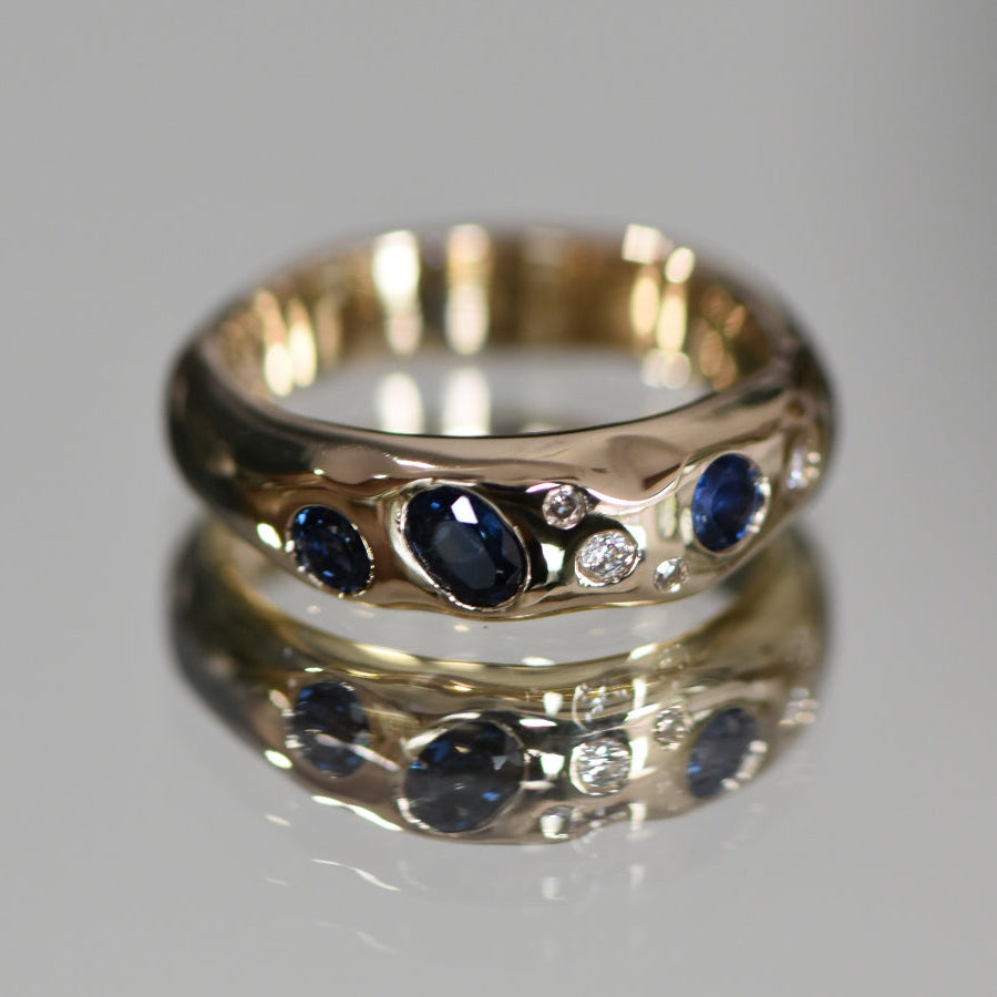 yellow gold ring with flush set blue sapphires on a gray background