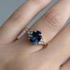 Close-up of a hand wearing a ring with a blue gemstone on a neutral background