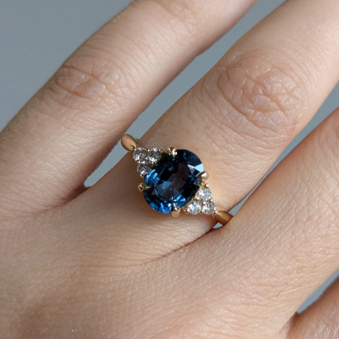 Close-up of a hand wearing a ring with a blue gemstone on a neutral background
