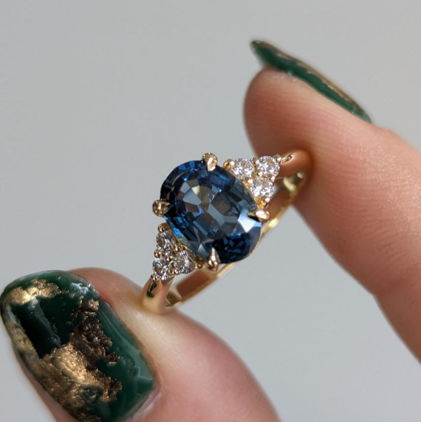 Gold ring with a blue gemstone held by a finger against a neutral background