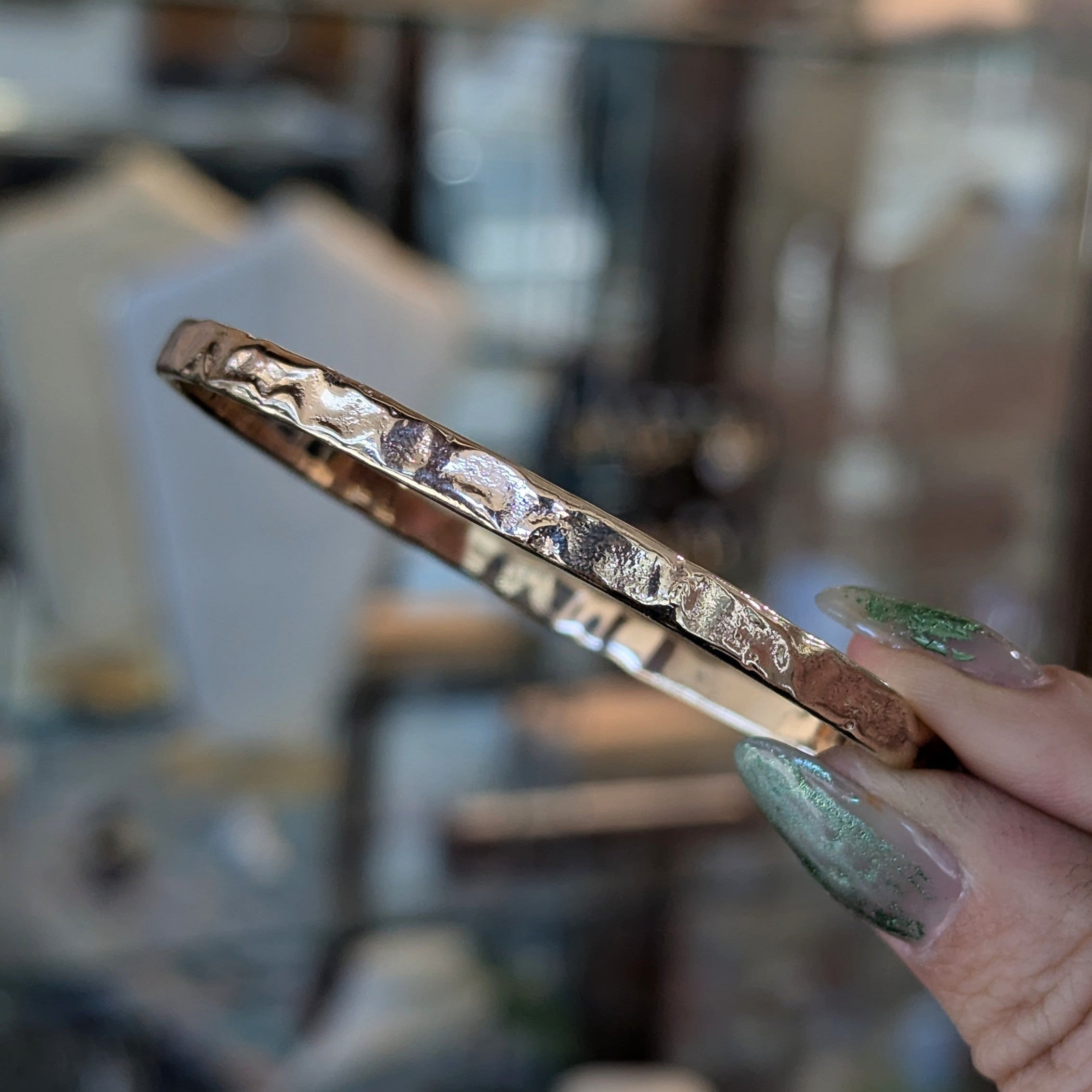 Yellow Gold reticulated bangle held by a hand with green nail polish against a blurred background