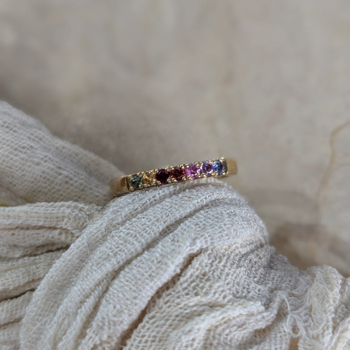 Gold ring with multicolored gemstones on a textured beige fabric background