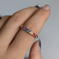 Ring with multicolored gemstones on a finger against a neutral background