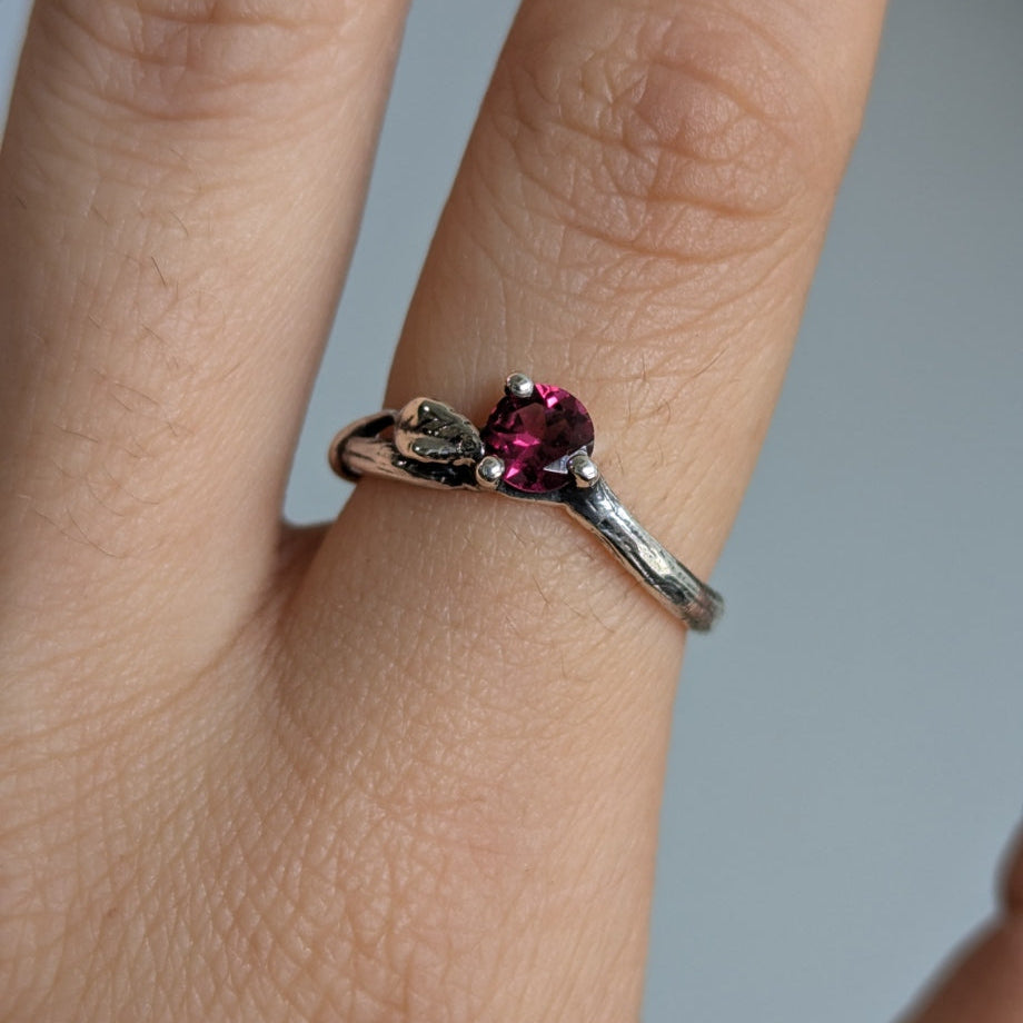 Silver ring with a red gemstone on a finger against a neutral background