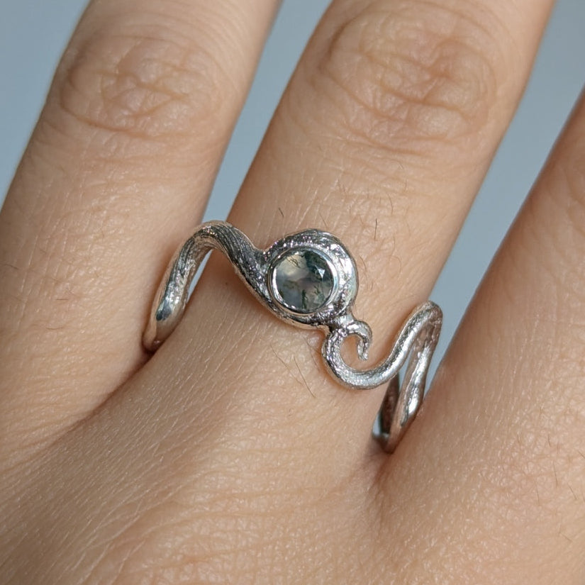 Silver ring with a gemstone on a finger against a neutral background
