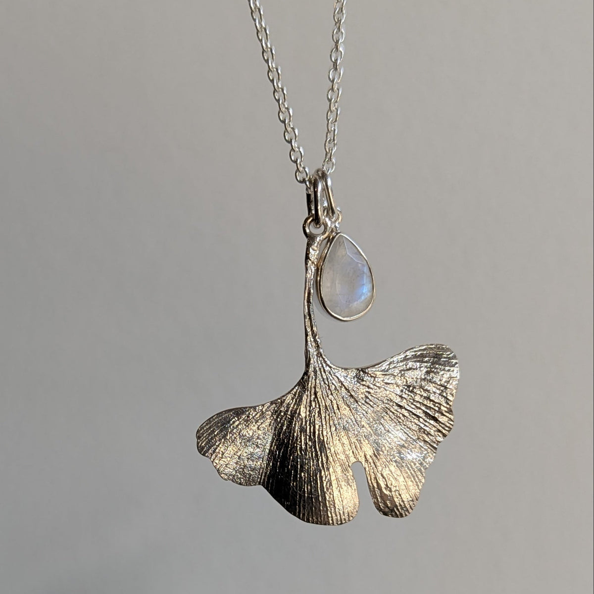 Silver pendant necklace with a leaf design on a gray background