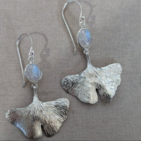 Silver ginkgo leaf earrings with moonstone stones on a gray background