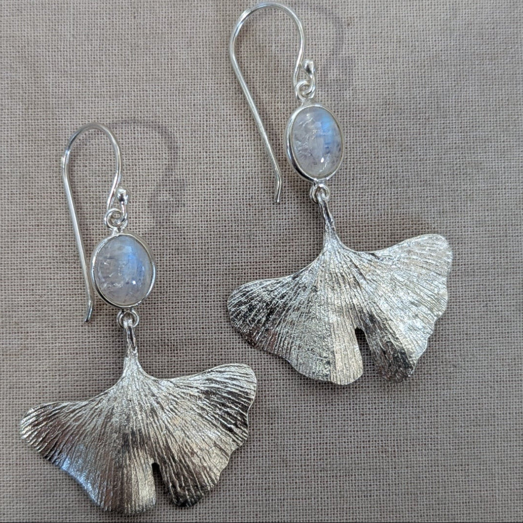 Silver ginkgo leaf earrings with moonstone stones on a gray background